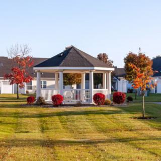 A picturesque gazebo surrounded by autumn trees and a neatly mowed lawn in a suburban area.