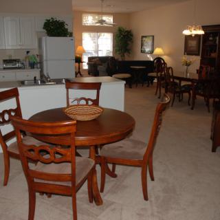 A cozy dining area with a wooden table and chairs, adjacent to a kitchen and living room.