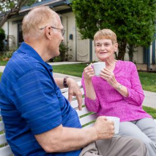 An elderly couple enjoying coffee and conversation on a park bench.
