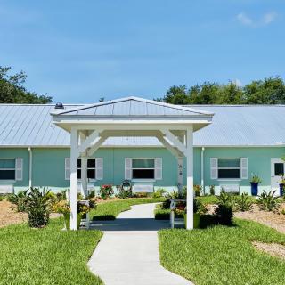 A light blue house with a white entrance, surrounded by a green lawn and garden.