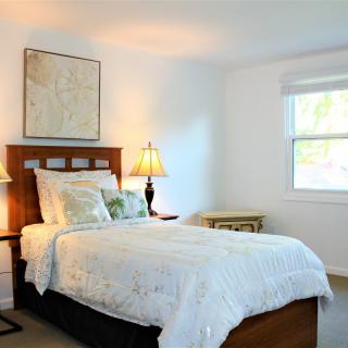 A cozy bedroom with a neatly made bed, decorated with lamps and natural light streaming through the window.