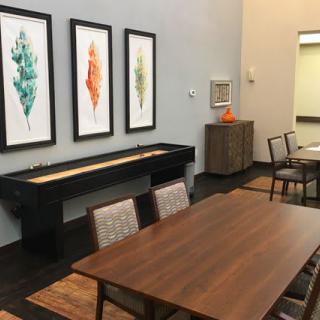 A modern dining room with a wooden table, chairs, and framed leaf artwork on the wall.