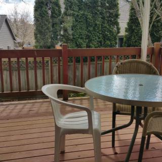 A wooden deck with a round table and chairs, surrounded by trees and a fence.