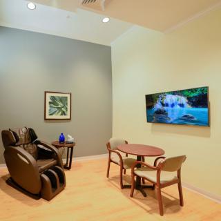 A cozy room featuring a massage chair, a small table with chairs, and a television mounted on the wall.