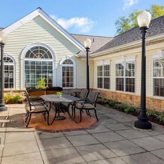A cozy outdoor patio with a table and chairs, surrounded by windows and lampposts.