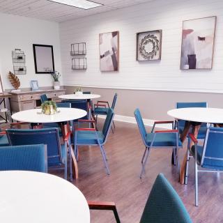 A modern office breakroom with round tables, blue chairs, and artwork on the walls.