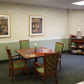 A cozy room with a table, four chairs, framed artwork, and a bookshelf.