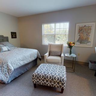 A modern bedroom with stylish decor, featuring a bed, comfortable chair, and patterned ottoman.