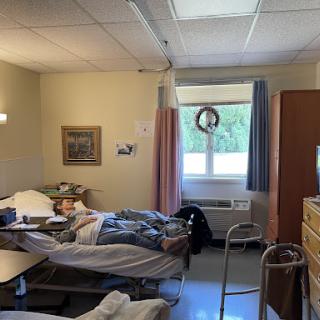 A view of a hospital patient room with two beds and windows letting in natural light.