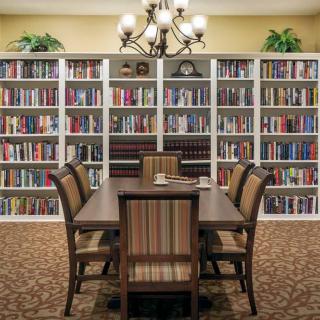 A cozy library setting with a wooden table and chairs surrounded by bookshelves filled with books.
