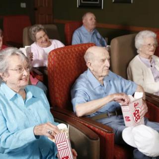 A group of senior citizens enjoying a movie at the theater with popcorn.