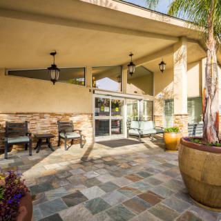 A welcoming building entrance featuring tile flooring, outdoor seating, and large planters.