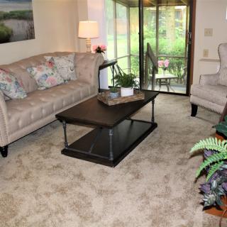 A cozy living room with a floral sofa, central coffee table, and a sliding glass door leading to an outdoor view.