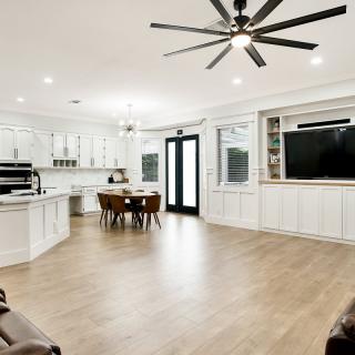 A spacious open-concept living and kitchen area featuring modern white cabinetry, a hardwood floor, and a large ceiling fan.