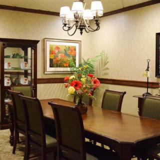 A formal dining room featuring a long wooden table with chairs, a chandelier overhead, and decorative elements including artwork and a floral centerpiece.