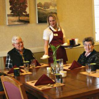 Two seniors dining at a restaurant with a waitress serving their table.