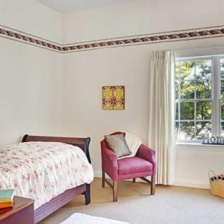 A cozy bedroom featuring a bed, a pink armchair, and a large window with curtains allowing natural light to fill the room.