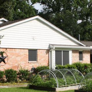 A residential house with a brick exterior and a small garden in the front yard.