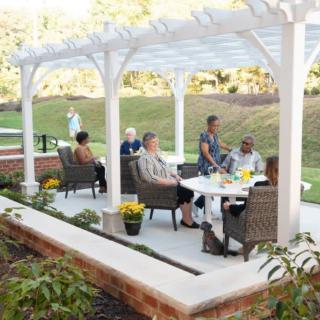 A group of people socializing under a pergola in a garden setting.