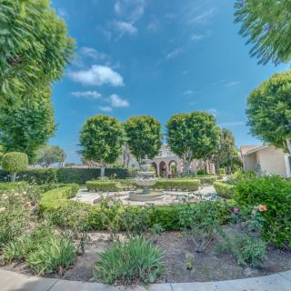 A serene garden with a central fountain surrounded by lush trees and vibrant greenery under a clear blue sky.