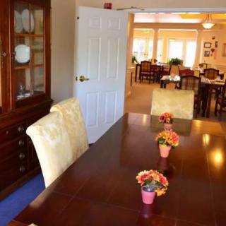 A dining room with a large wooden table, decorated with small flower arrangements, accompanied by upholstered chairs and a wooden cabinet in the background.