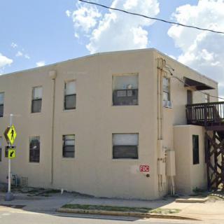 A two-story apartment building with exterior stairs and multiple windows on a sunny day.