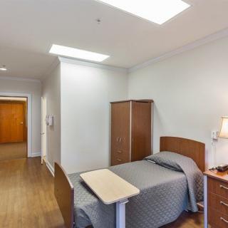 A hospital room featuring a single bed, a wardrobe, and a bedside table with a lamp.