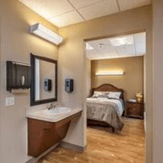 A cozy bedroom with an attached sink and mirror area, featuring warm lighting and wood flooring.
