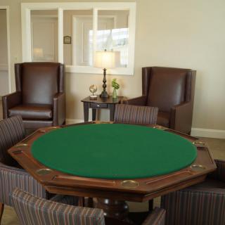 A cozy game room with a green felt poker table surrounded by chairs and elegant decor.