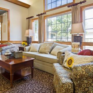 A cozy living room with a sofa and patterned armchairs, illuminated by natural light from large windows.