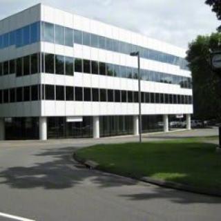 Modern office building with glass windows and a minimalist design surrounded by greenery.