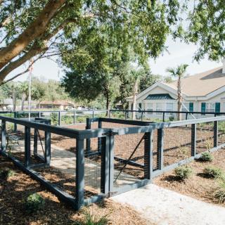 An outdoor dog park with fencing and trees, featuring a pathway through the landscaped area.