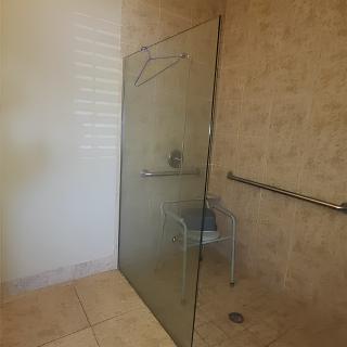 A spacious bathroom with a glass-partitioned shower, featuring a handrail for accessibility.