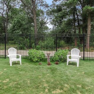 Two white chairs in a garden setting alongside a black fence and lush greenery.