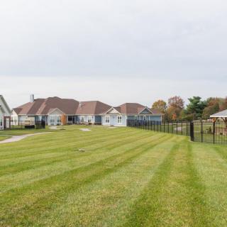 A view of suburban houses with a neatly maintained lawn and fence under a cloudy sky.