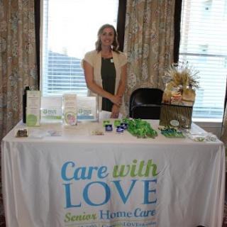 A representative stands at a booth promoting 'Care with Love' services at an event.