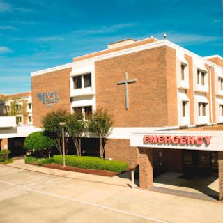 A view of a medical facility featuring emergency services and a prominent Christian cross.
