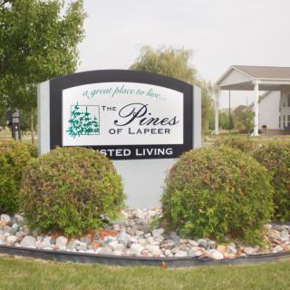 Sign for The Pines of Lapeer Assisted Living surrounded by landscaping.