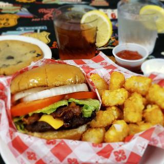 A delicious meal featuring a burger with tater tots, a cookie, and a refreshing drink.