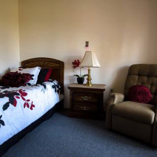 A cozy bedroom corner featuring a bed with floral bedding, an armchair, and a nightstand with a lamp.