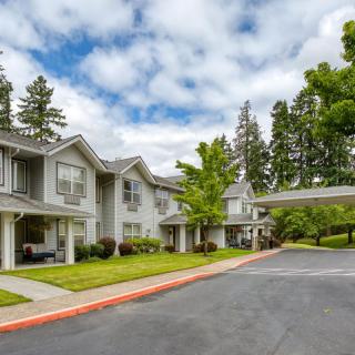 A residential apartment complex with a driveway surrounded by trees and an overcast sky.