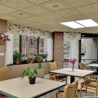 A cozy dining area in a senior living facility, adorned with plants and filled with natural light.