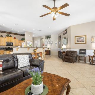 Spacious open-concept living area with a view of the kitchen, featuring brown leather sofas, a ceiling fan, and tile flooring.