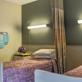 A hospital room featuring two twin beds with curtains for privacy and a bedside table adorned with flowers.