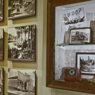 A collection of vintage black and white photographs displayed on a wall, accompanied by an antique camera in a museum setting.