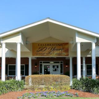A welcoming entrance to a community center, featuring well-maintained landscaping and a clear blue sky.