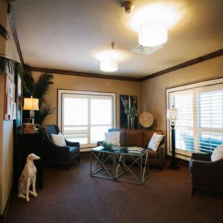 A cozy living room with modern furniture and decor, featuring a sofa, armchairs, a glass coffee table, and large windows.
