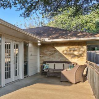 A cozy patio area with outdoor seating, located outside a house with French doors and surrounded by lush trees.