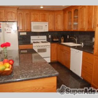 A modern kitchen with wooden cabinets and granite countertops, equipped with various appliances including a stove, microwave, refrigerator, and dishwasher.