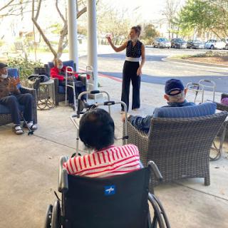 A community event where a speaker engages with seniors in an outdoor setting, promoting social interaction and well-being.